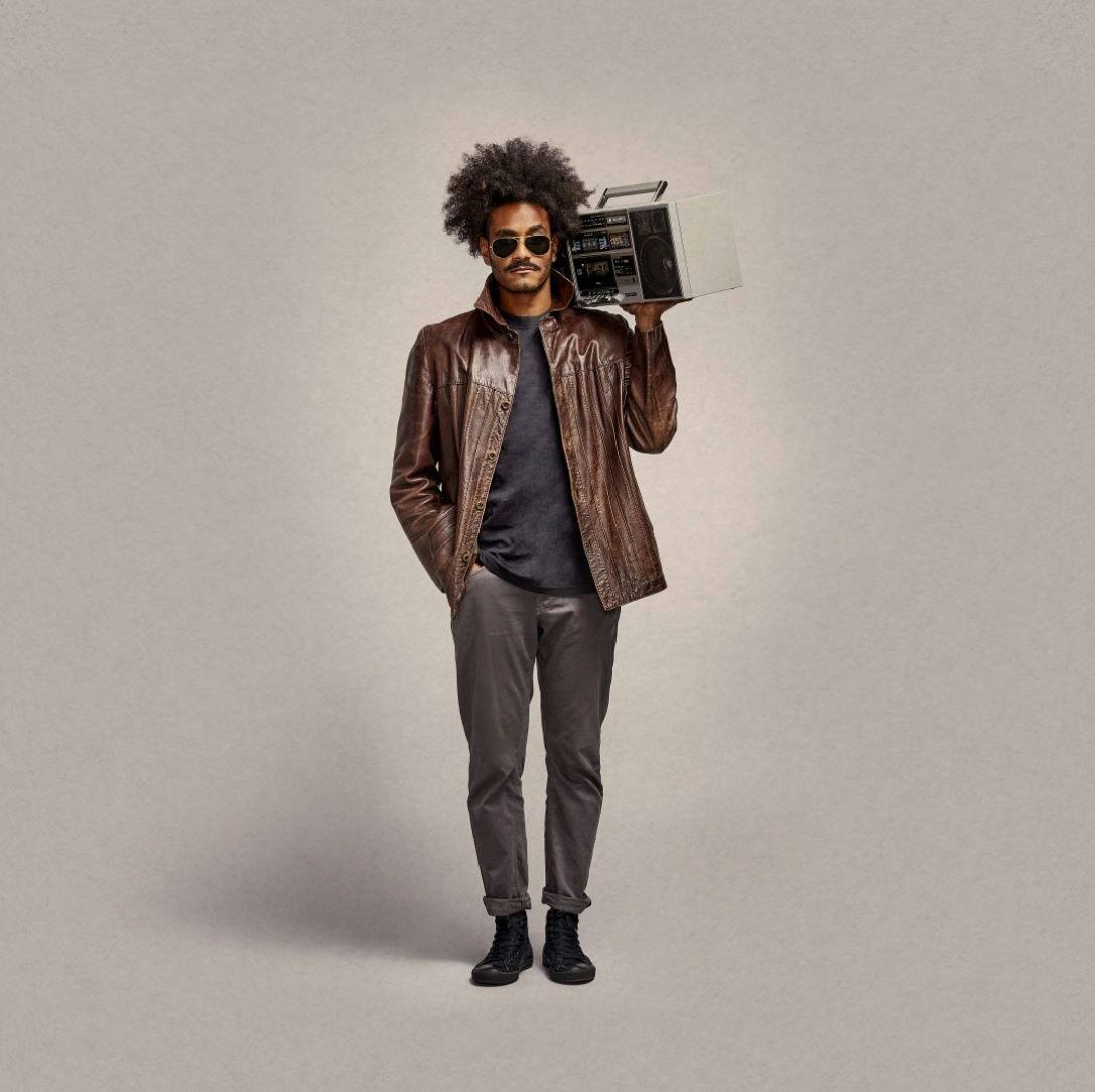 Man with afro and leather jacket holding an old school boombox over his shoulder